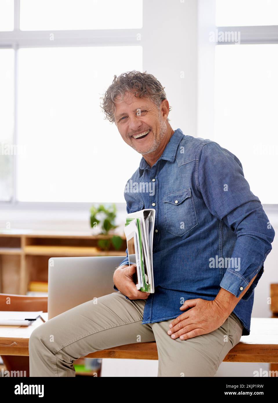 Ich habe mich nach oben gearbeitet. Porträt eines erwachsenen Geschäftsmanns, der Papierkram hält, während er auf seinem Schreibtisch sitzt. Stockfoto