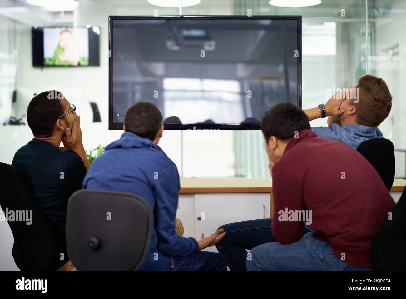 Als Team die Qual der Niederlage zu spüren. Rückansicht einer Gruppe schockierter junger Männer, die einen Montior betrachten. Stockfoto