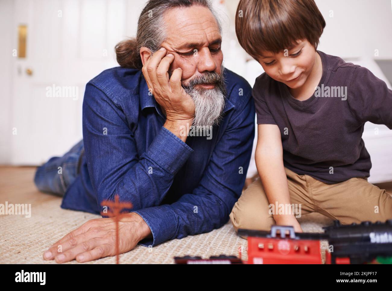 Erinnerungen an seine Kindheit. Ein Großvater, der seinem Enkel beim Spielen mit einem Spielzeugzug zusieht. Stockfoto