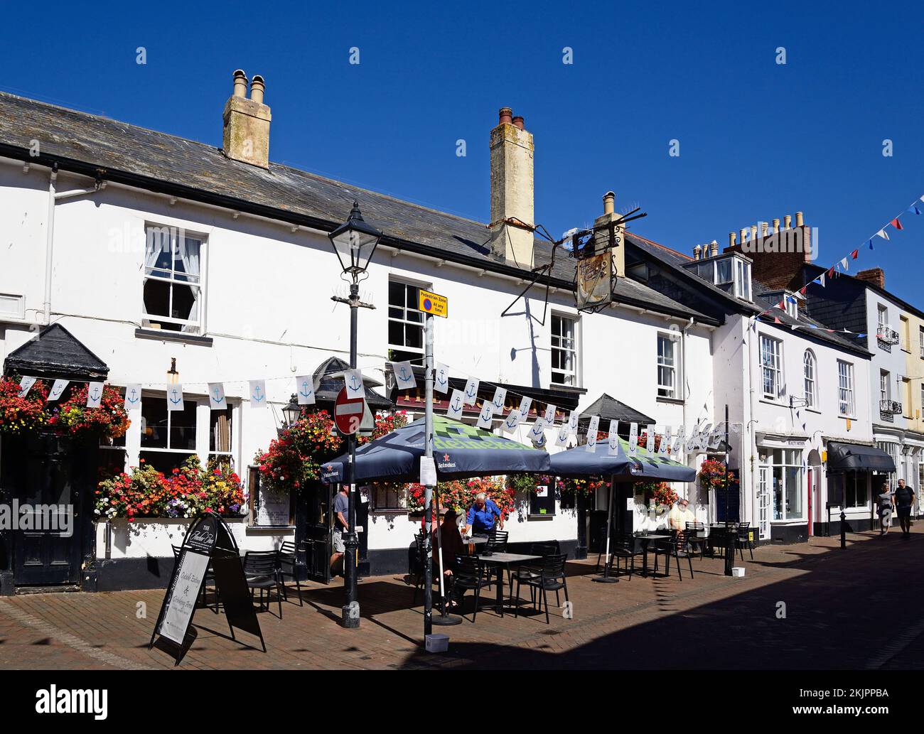 Touristen entspannen sich an Tischen vor dem Anchor Inn entlang der Old Fore Street im Stadtzentrum, Sidmouth, Devon, Großbritannien, Europa. Stockfoto