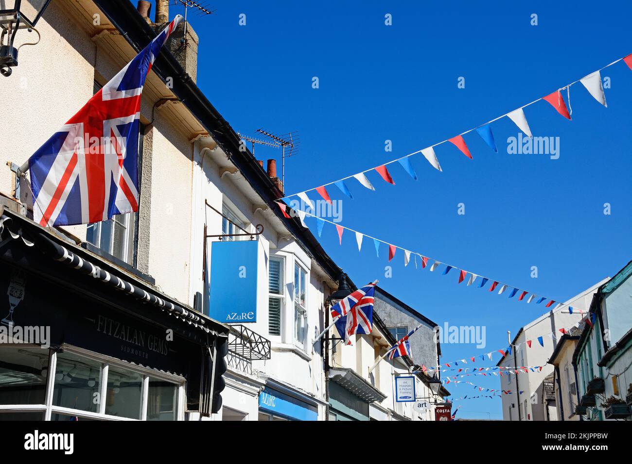 Traditionelle Ladengebäude und Flaggen entlang der Old Fore Street im Stadtzentrum, Sidmouth, Devon, Großbritannien, Europa. Stockfoto