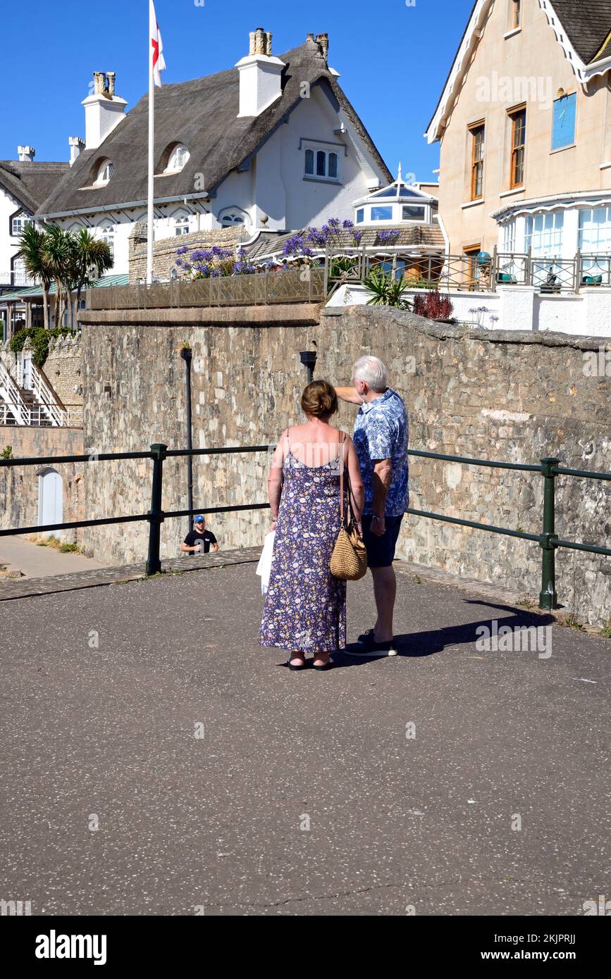 Blick auf strohgedeckte Häuser mit Blick auf den Strand, ein Paar steht im Vordergrund, Sidmouth, Devon, Großbritannien. Stockfoto