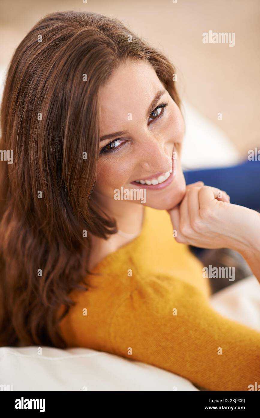 sonniges sonntagslächeln. Porträt einer Frau, die drinnen sitzt und ihren Kopf auf der Hand ruht. Stockfoto