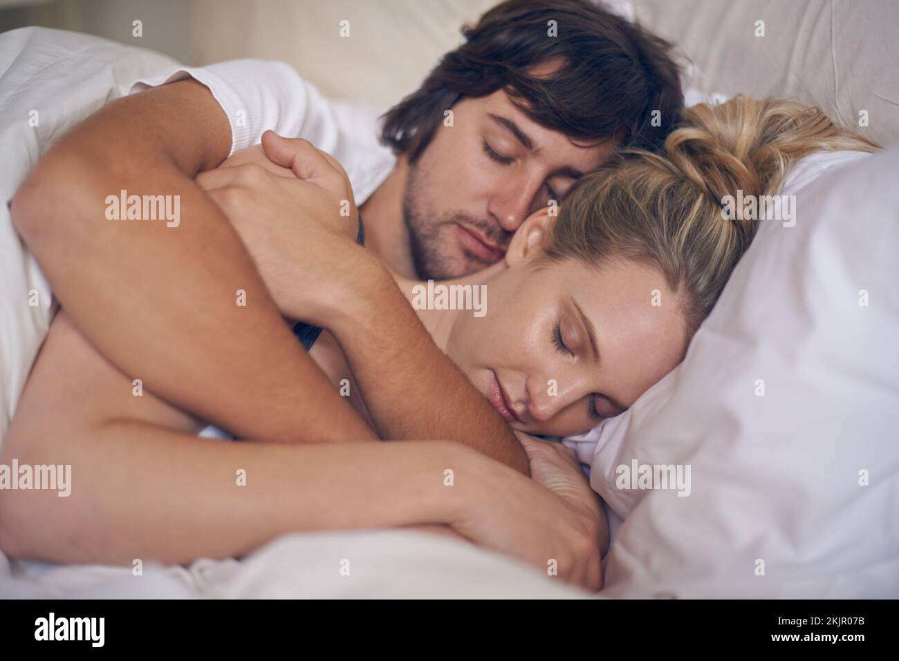 Eingewickelt in seine Liebe. Ein liebevolles junges Paar, das im Schlaf kuschelt. Stockfoto
