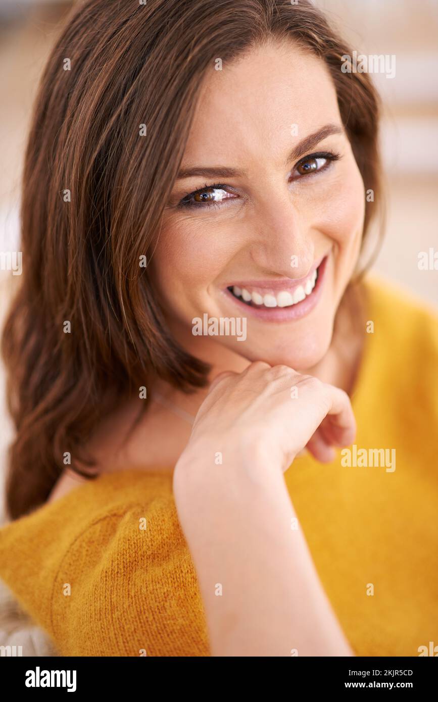Lächeln Sie, als ob Sie es ernst meinen. Porträt einer Frau, die drinnen sitzt und ihren Kopf auf der Hand ruht. Stockfoto