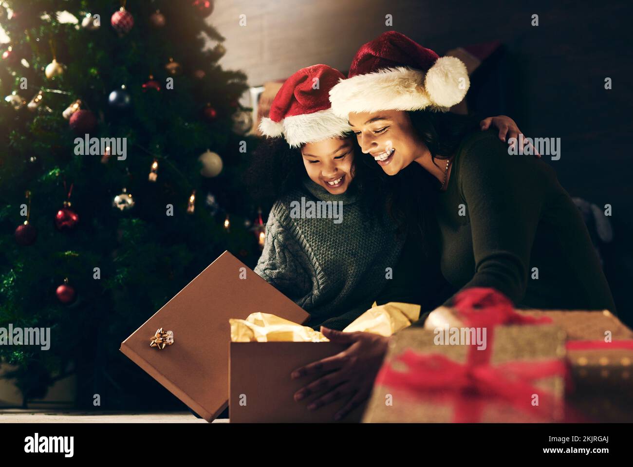 Nacht, Mutter und Kind mit einem Weihnachtsgeschenk zur Feier eines glücklichen Familienurlaubs im Winter zu Hause. Liebe, gebend und verließ mom, die eine öffnete Stockfoto