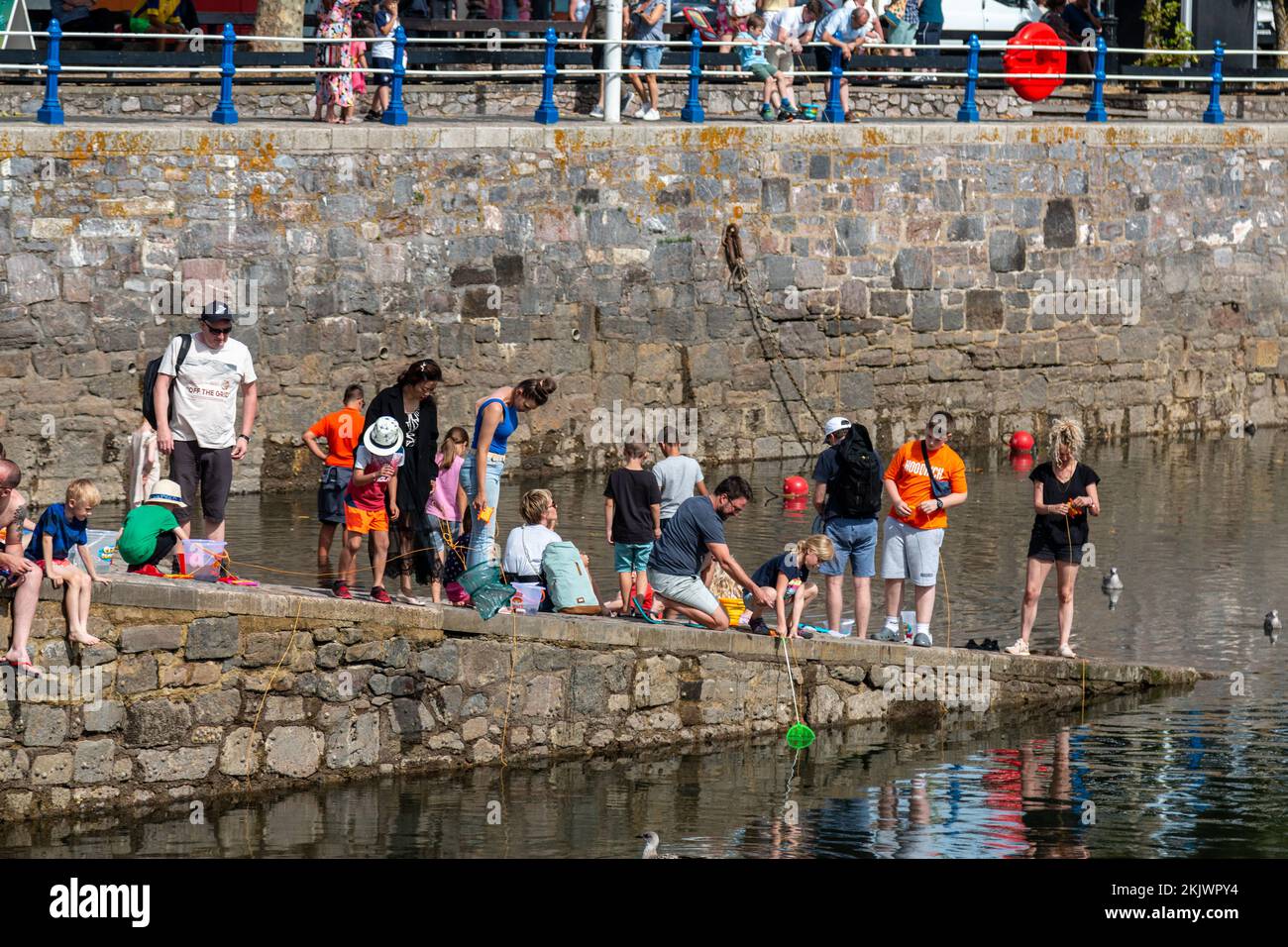 Urlauber, die Krabben auf der Slipway des Torquay Harbour angeln. Stockfoto