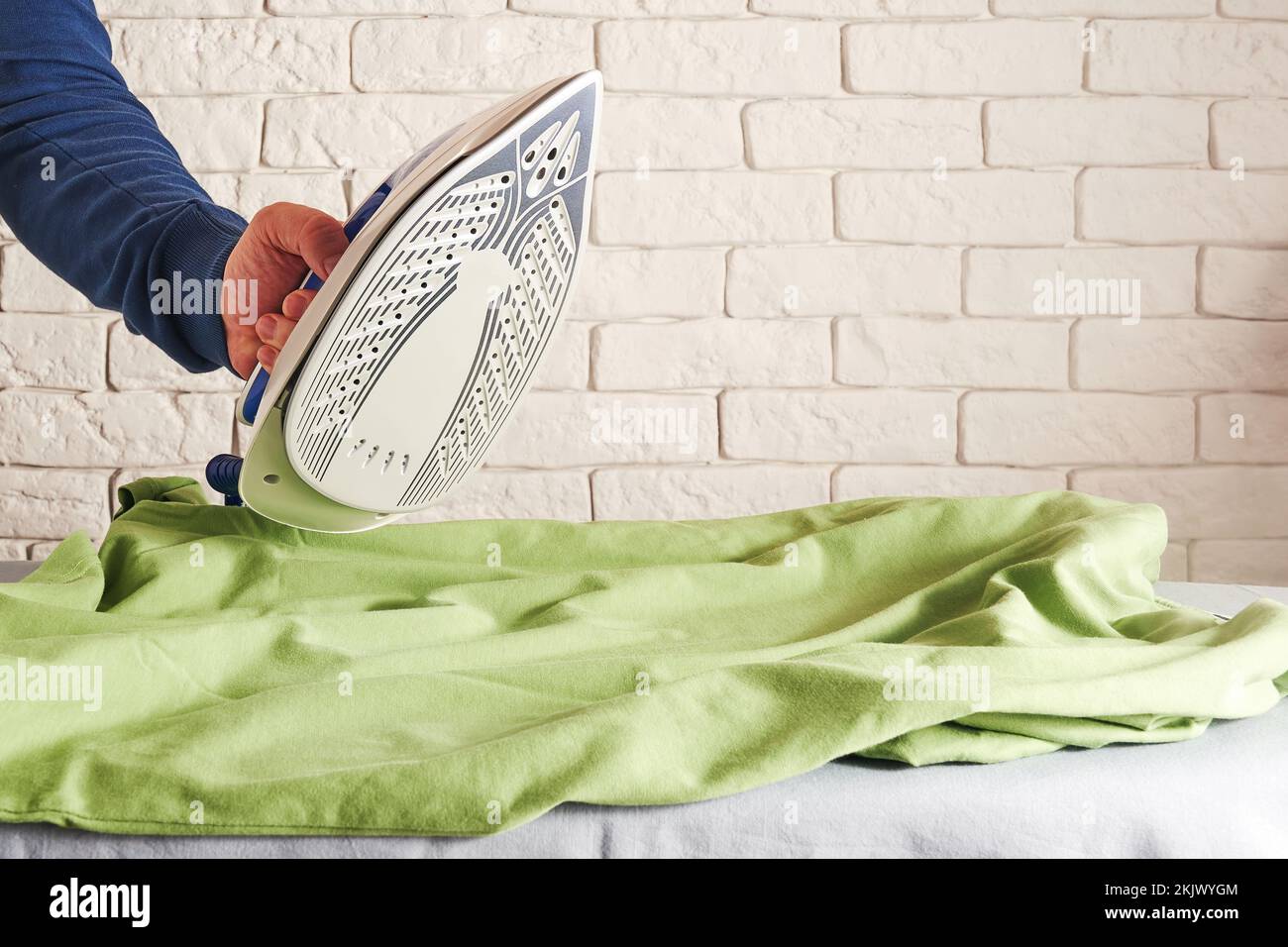 Männerhand mit heißem Eisen und glättet faltiges grünes Hemd. Haushaltsarbeit und Wäscheservice. Platz für Text kopieren Stockfoto