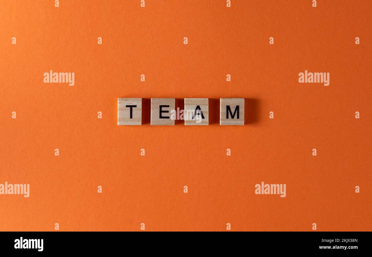 Teamwortsatz in Holzbuchstaben. Motivation und Slogan. Orangefarbener Hintergrund. Stockfoto