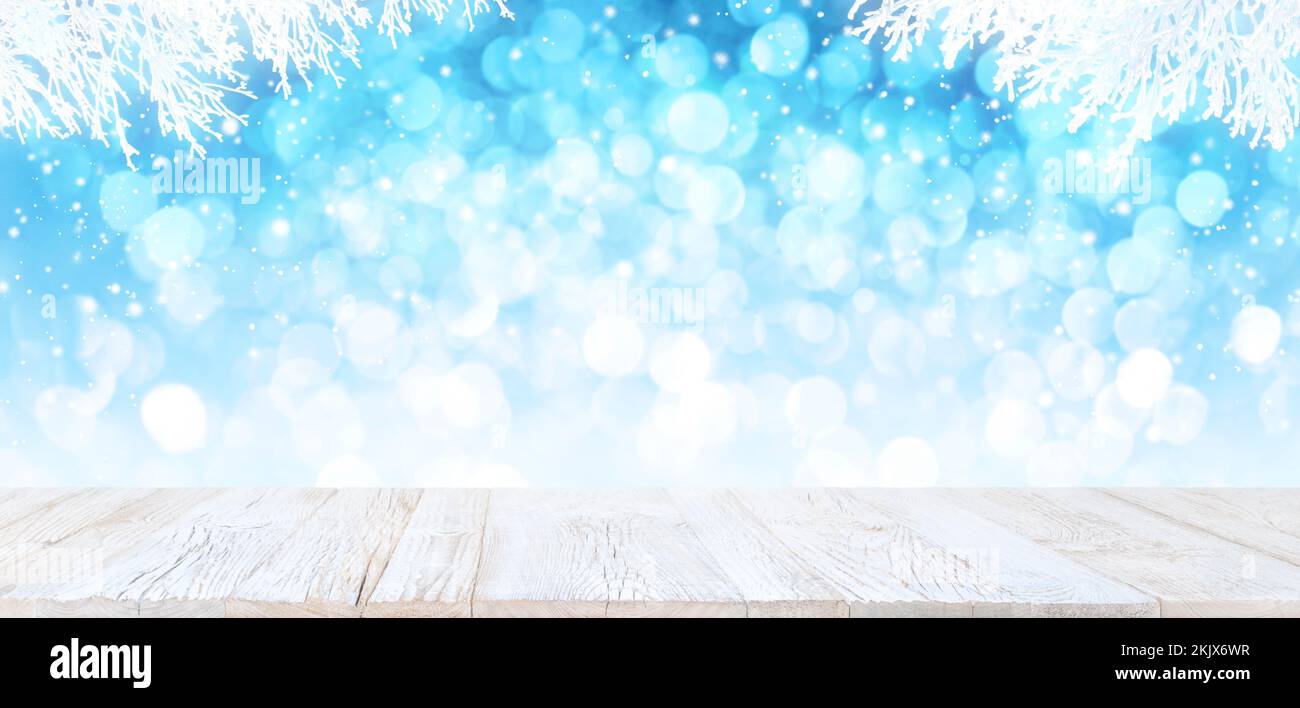 Ein alter weißer Holztisch im Vintage-Stil mit Blick auf den hellblauen Bokeh-Winterhintergrund mit weißen schneebedeckten Ästen und herabfallendem Schnee. Produktdisplay Stockfoto