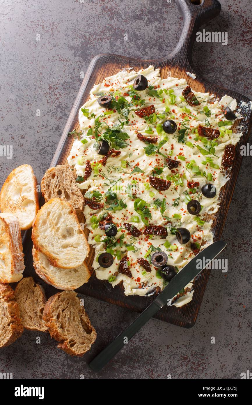 Hausgemachtes, trendiges Butterboard mit Kräutern, Oliven, sonnengetrockneten Tomaten und Brot auf dem Tisch. Vertikale Draufsicht von oben Stockfoto