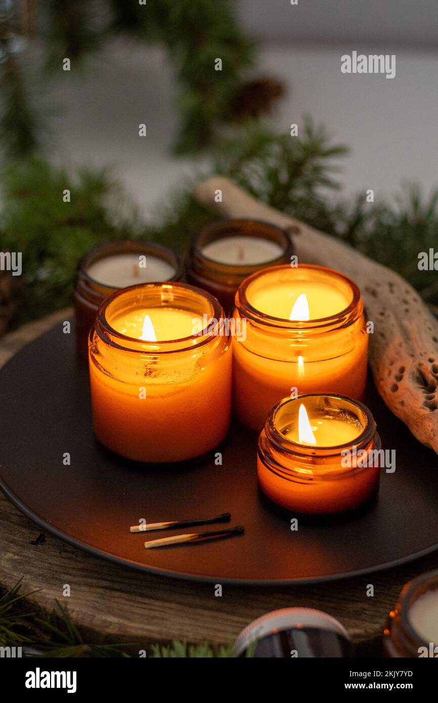 Sojalkerzen brennen in Gläsern. Komfort zu Hause. Kerze in einem braunen Glas. Duft und Licht. Handgemachte Duftkerze. Aromatherapie. Weihnachtsbaum und Winterstimmung. Gemütliche Einrichtung. Festliche Dekoration Stockfoto