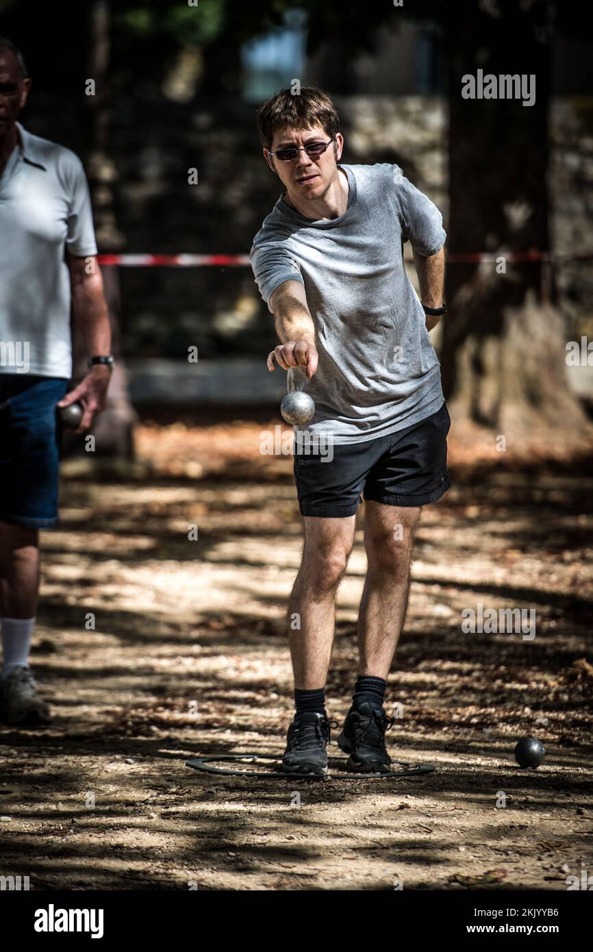 Ein Spieler wirft einen Ball, Boule während eines traditionellen französischen Pétanque-Spiels auf dem Dorfplatz Stockfoto