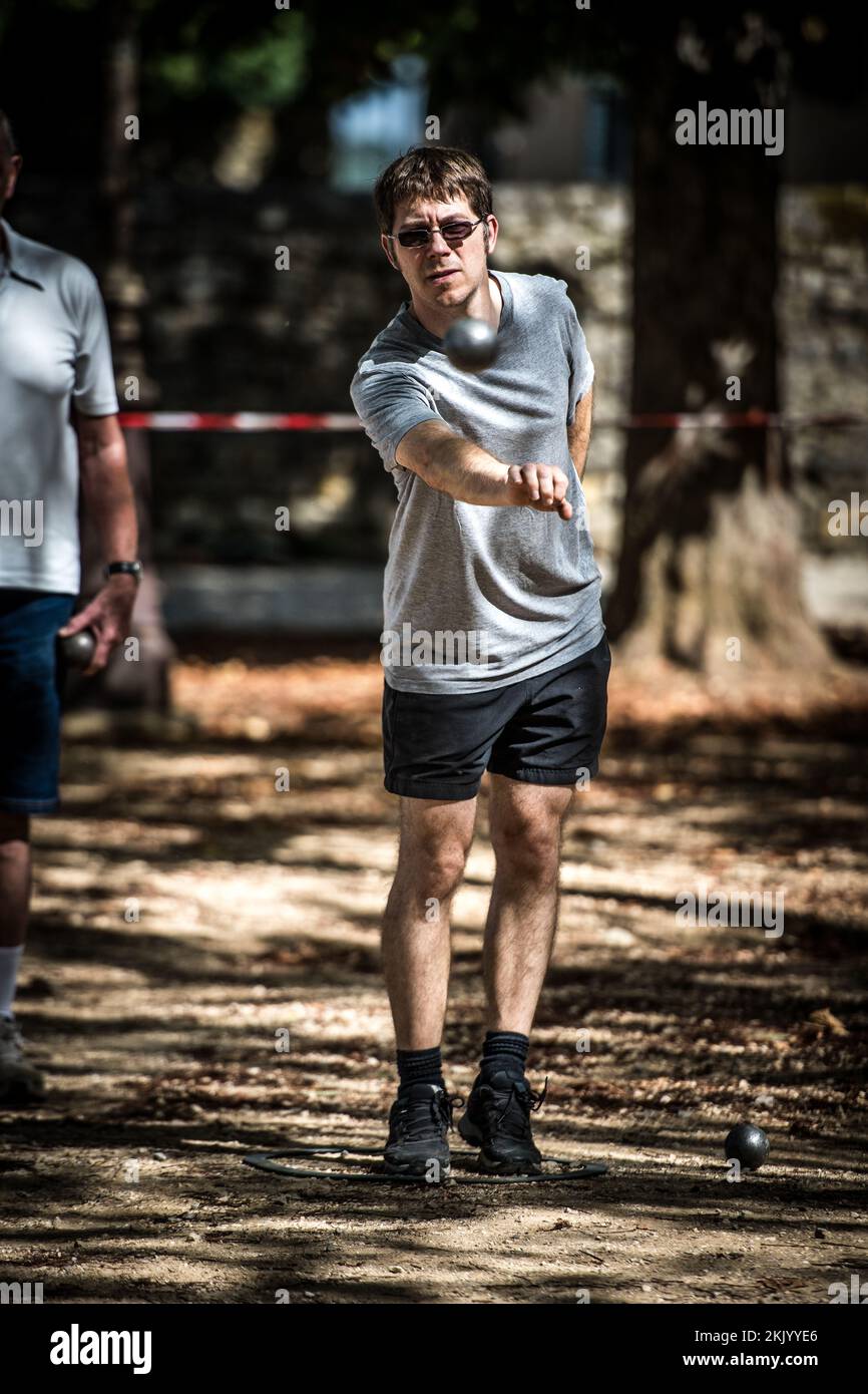 Ein Spieler wirft einen Ball, Boule während eines traditionellen französischen Pétanque-Spiels auf dem Dorfplatz Stockfoto