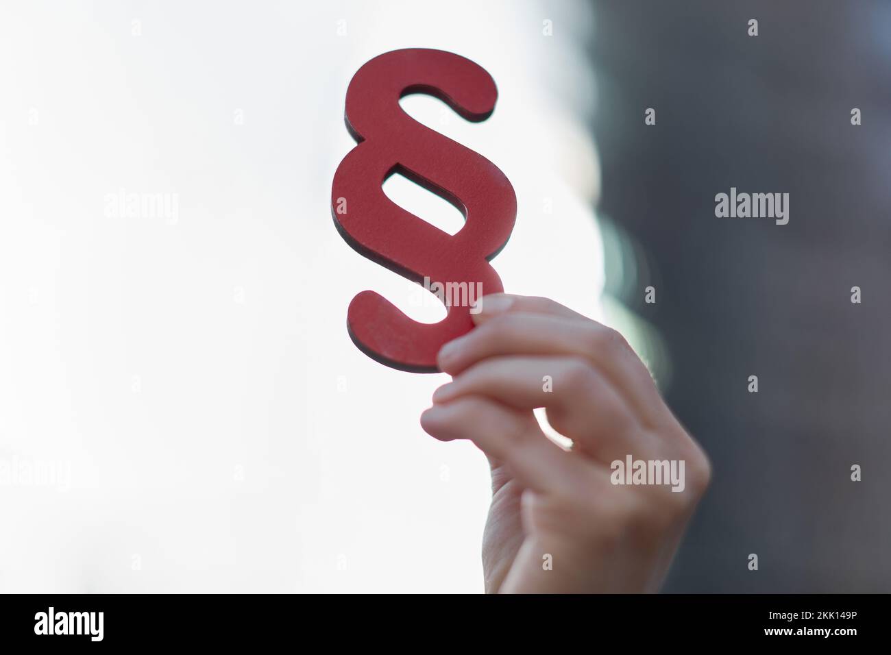 Hand einer Geschäftsfrau, die das Paragraphensymbol als Rechtsbegriff vor dem Himmel hält Stockfoto