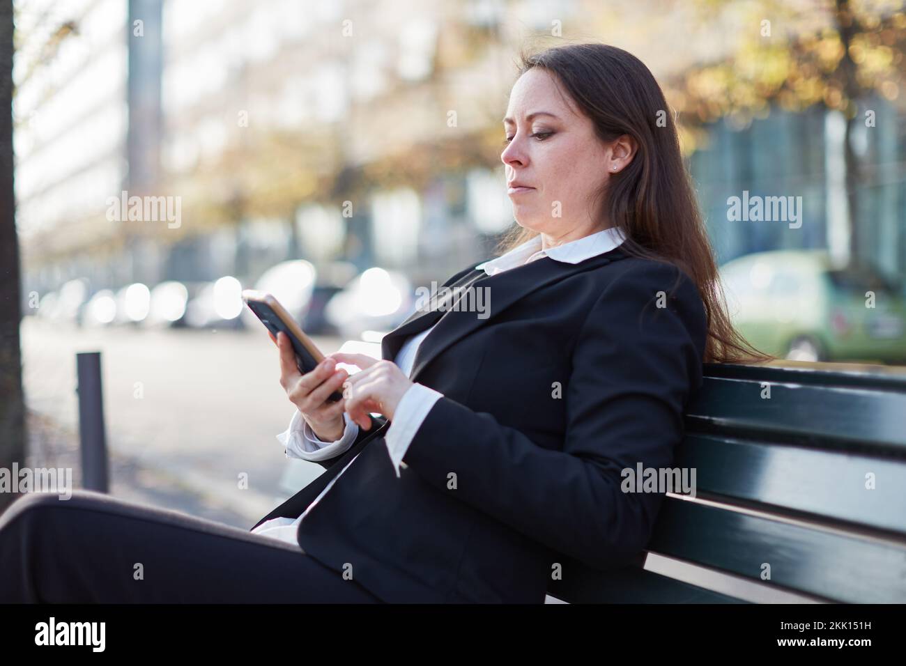 Geschäftsfrau, die in der Stadt auf einer Bank sitzt und ihr Smartphone für SMS und Chats nutzt Stockfoto