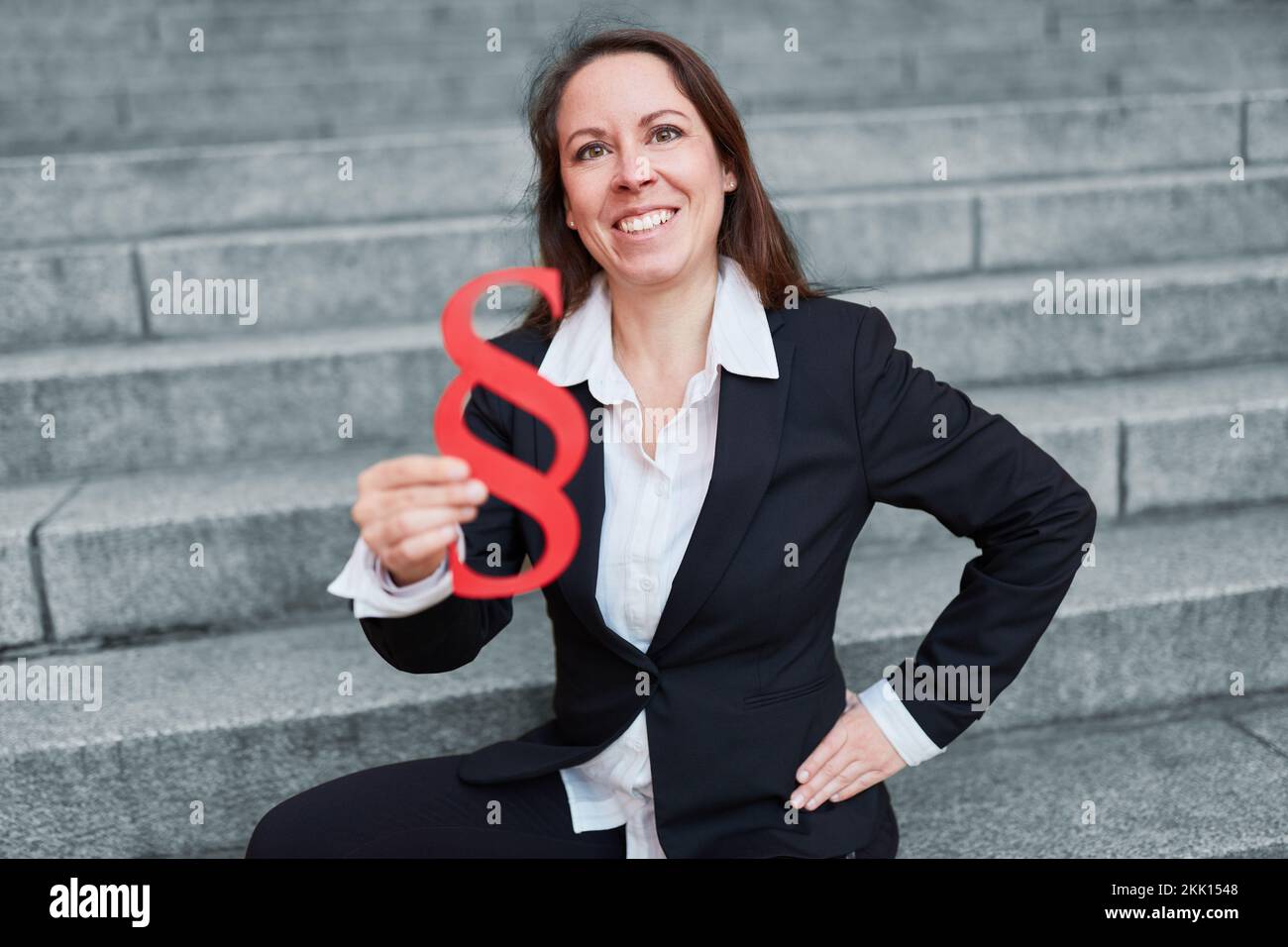 Lächelnde, glückliche Anwältin, die ein rotes Absatzzeichen als Gerechtigkeit- und Rechtssymbol hält Stockfoto