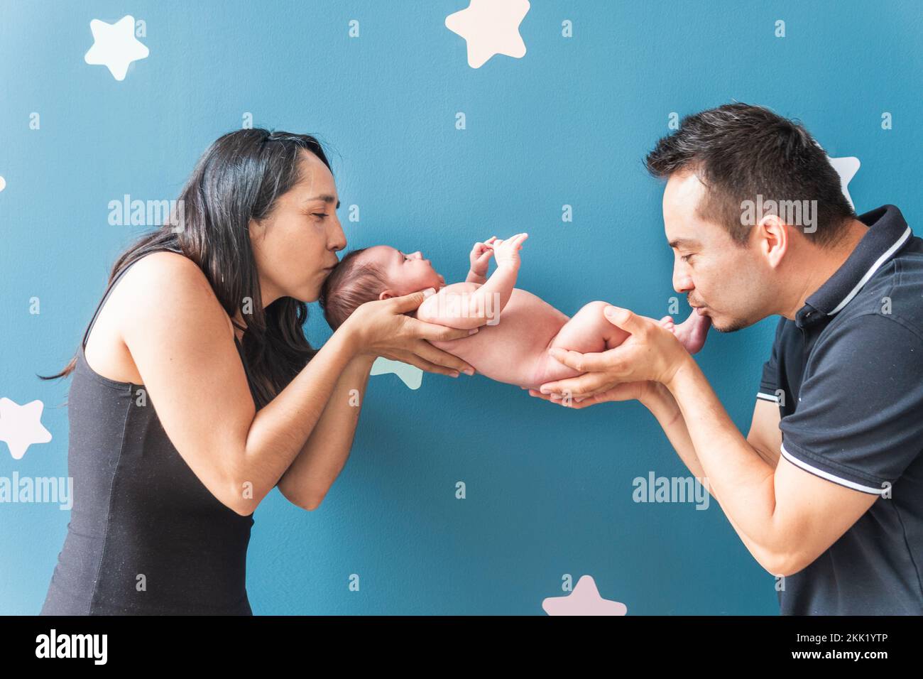 Lateinamerikanische Mutter und Vater halten ihr Baby in den Händen und geben ihm einen Kuss Stockfoto