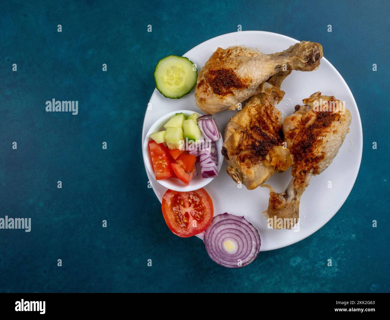 Im Ofen gebratenes Hähnchen Trommeln Beine Zecken auf einem weißen Teller mit einem gesunden Beilagensalat auf türkisfarbenem Hintergrund Stockfoto