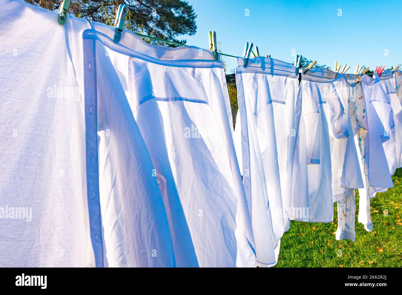 Weiße Hemden und Kleider trocknen an einem klaren, sonnigen Herbsttag an einer Wäscheleine mit blauem Himmel. Stockfoto
