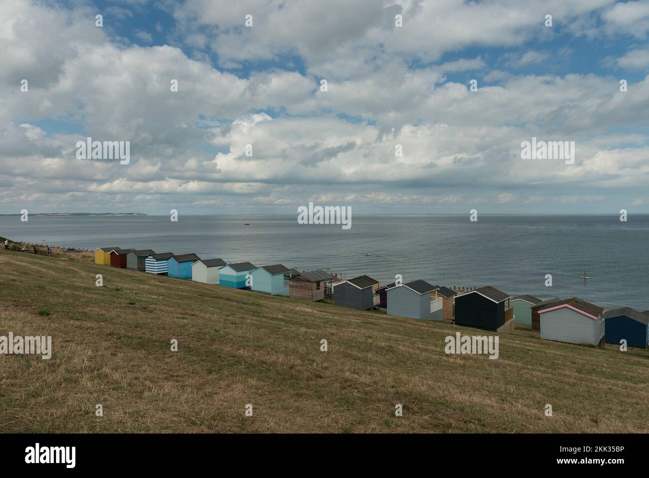 Schöne gepflegte Strandhütten an einem muscheligen Sommertag zur Hochsaison, um sich gegen den wechselnden bewölkten Himmel und das ruhige Meer zu reflektieren Stockfoto