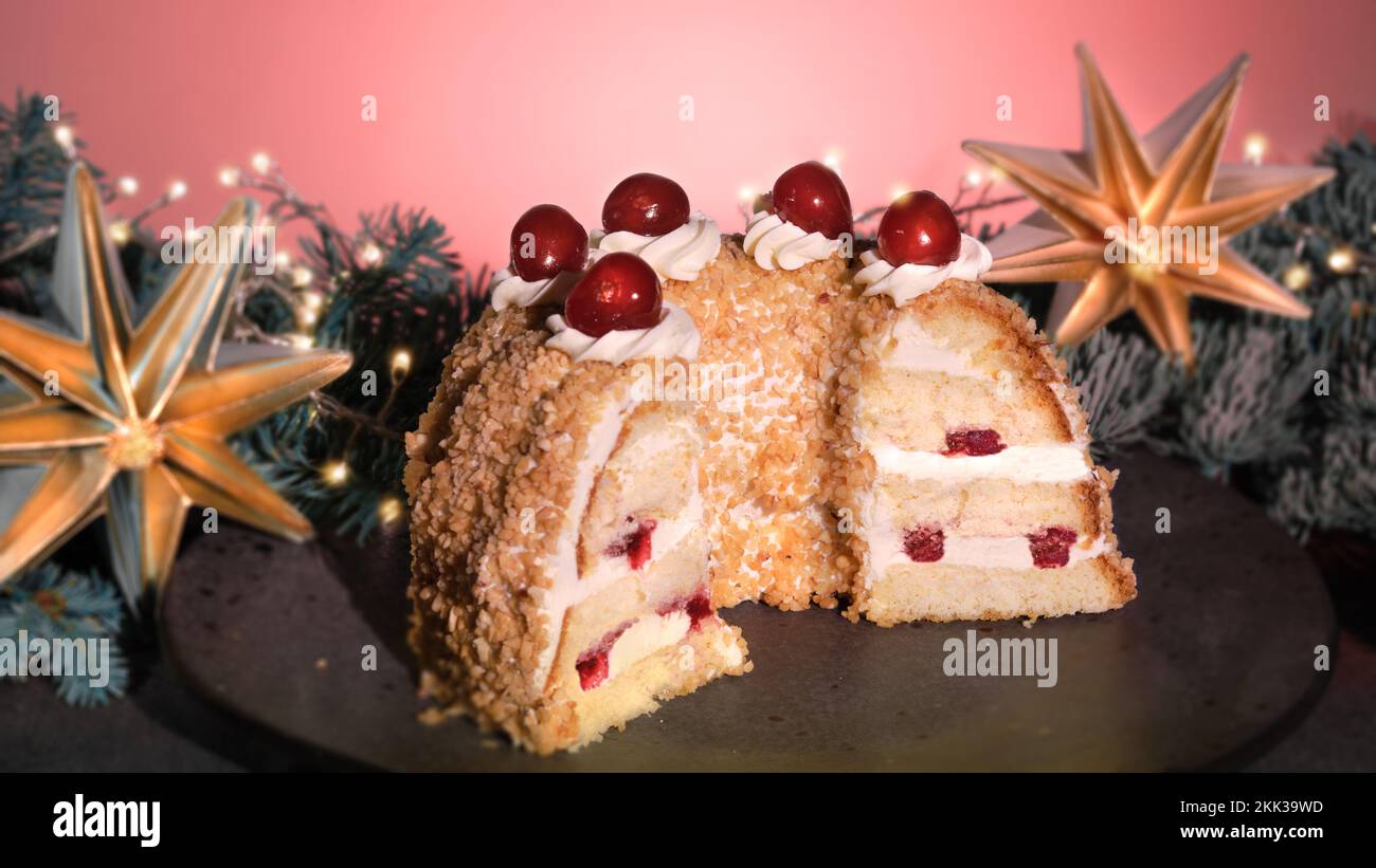 Deutsche Kuchen Frankfurter Kranz oder Frankfurter Crown Cake. Bisquit mit Buttercreme, Kirsche. Die Hälfte des Kuchens auf schwarzem Teller. Schwarzer und rosafarbener Hintergrund Stockfoto