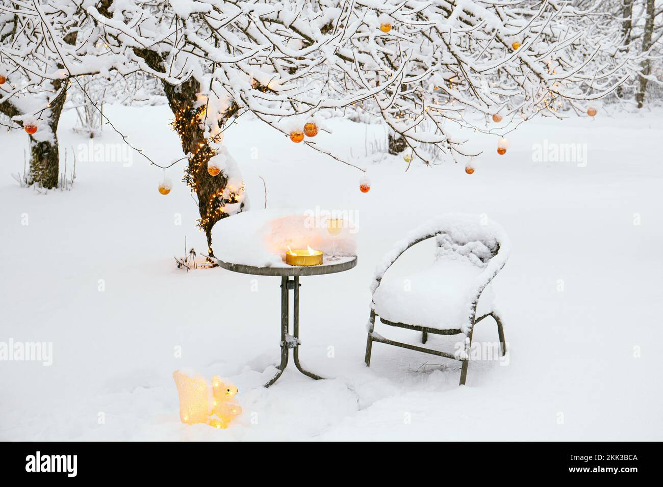 Im Winter verschneite Apfelbäume im Garten, dekoriert mit vielen kupferfarbenen metallischen Weihnachtskugeln und warmweißen LED-Lichtern mit Schnur. Stockfoto