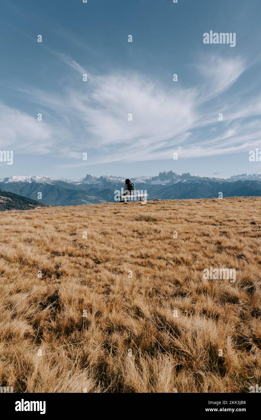 Eine Frau sitzt auf einer kleinen Bank in den Bergen und betrachtet die Dolomiten in der Ferne. 1 Stockfoto