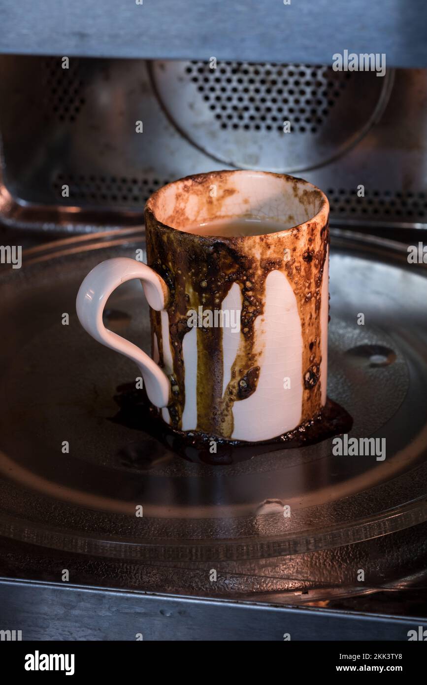 Verschüttetes Kaffeegetränk lief in der Mikrowelle über und verursachte so ein großes Chaos, das weggeräumt wurde, weil es vergessen wurde, und legte die falsche Einstellung ein, um zu viele Dinge beim Multitasking zu jonglieren Stockfoto