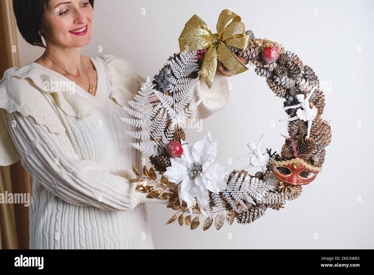 Nahaufnahme Frau hängt wunderschönen Weihnachtskranz. Die Basis des Kranzes sind Fichtenäste, keine verschwenderische Dekoration in weiblichen Händen Stockfoto