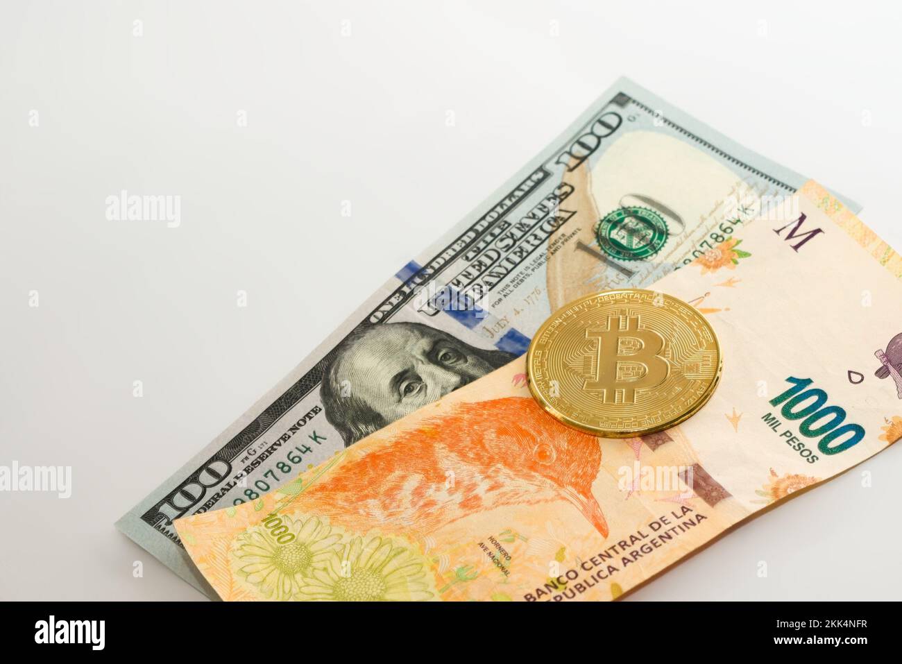 Physische Bitcoin über hundert Dollar und tausend argentinische Pesos. Währungsumtausch, internationales Investitionskonzept. Stockfoto