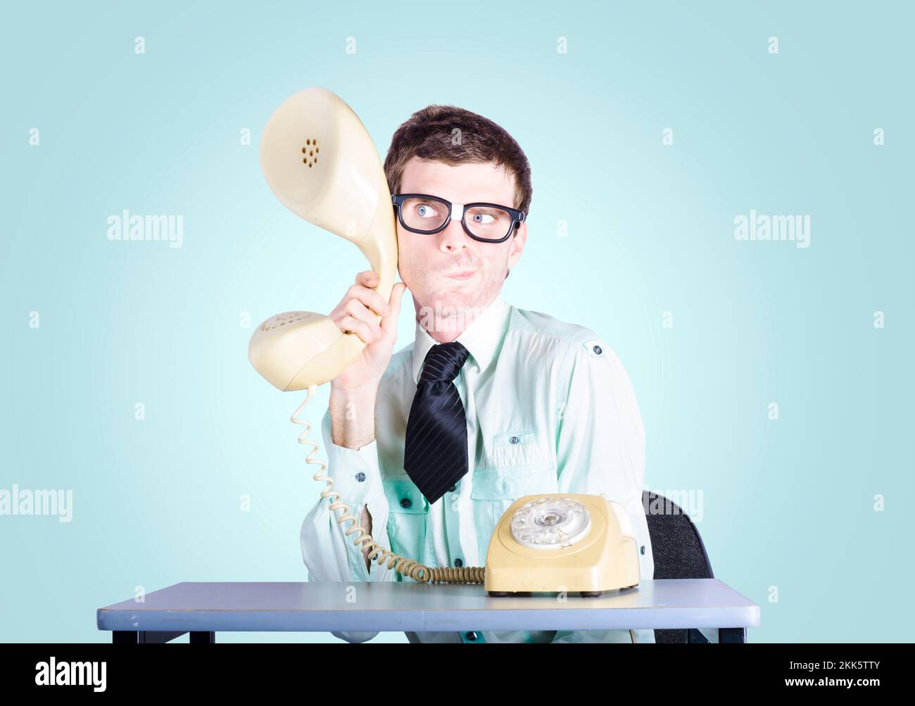 Bild eines Nerd-Geschäftsmannes, der an einem Schreibtisch sitzt und einen vergrößerten Telefonhörer hält, um Informationen über die Konkurrenz abzufangen. Marktforschungskontra Stockfoto