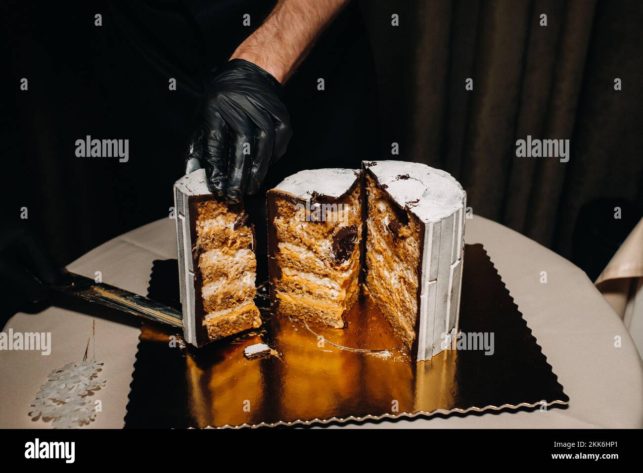 Fantastische Kuchen. Ein Koch mit schwarzen Handschuhen schneidet eine Schokoladenkuchen-Hochzeitstorte auf. Der Hochzeitskuchen ist innen köstlich auf schwarzem Hintergrund. Großer Kuchen in Weiß Stockfoto