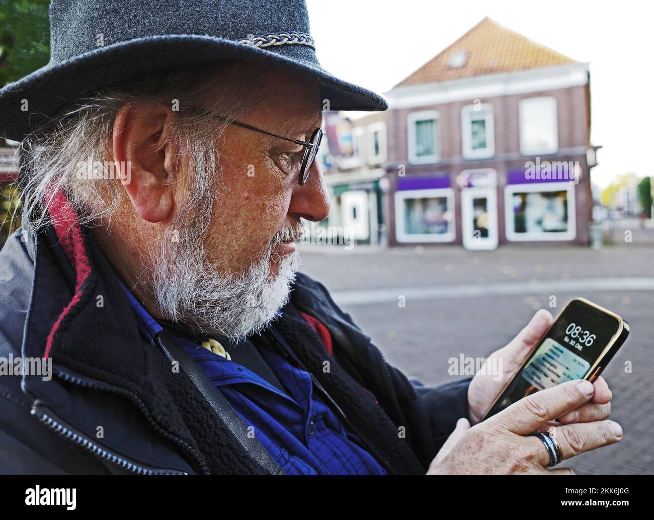 Ein älterer Mann mit Hut überprüft sein Smartphone. Er befindet sich mitten in der historischen Stadt Coevorden in den Niederlanden Stockfoto