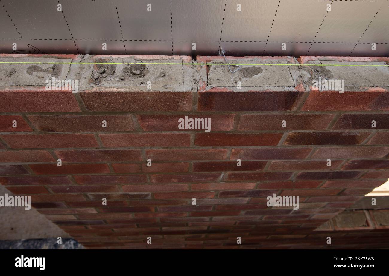 Nahaufnahme einer teilweise gebauten roten Ziegelwand mit sichtbarem Mörtel und Ausrichtfaden während der Bauarbeiten Stockfoto