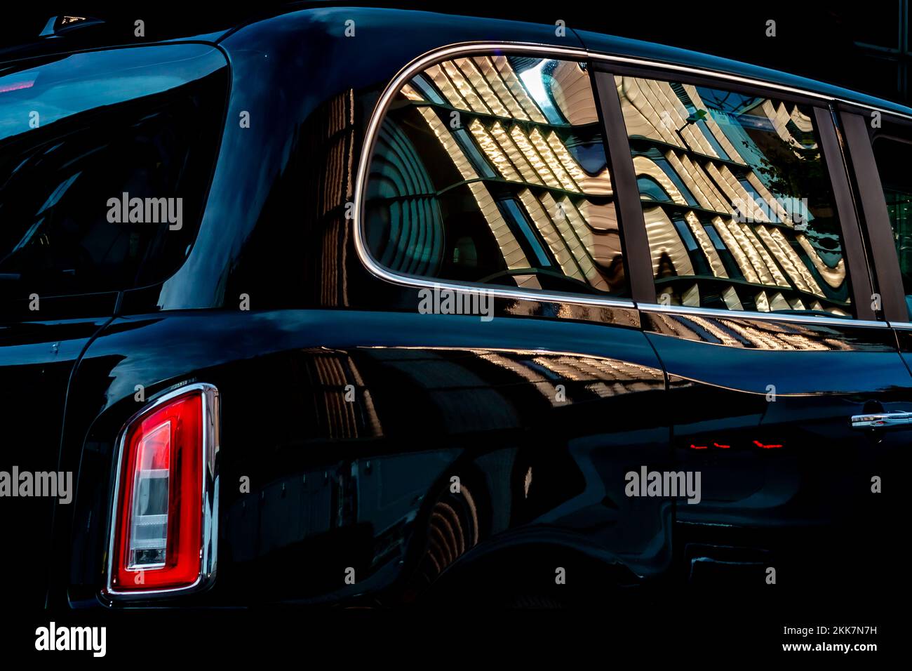 Ein neues Black Taxi Cab mit einem glänzenden neuen Gebäude, das sich in der hochpolierten Karosserie widerspiegelt. Dies ergibt ein überzeugendes redaktionelles Bild. Seitenansicht. Stockfoto