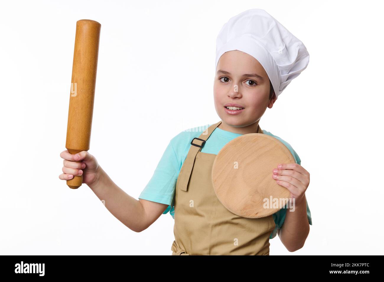 Niedlicher Junge, mit Köchmütze und Schürze, Posen mit einem Drehstift und Holzbrett, auf weißem Hintergrund Stockfoto