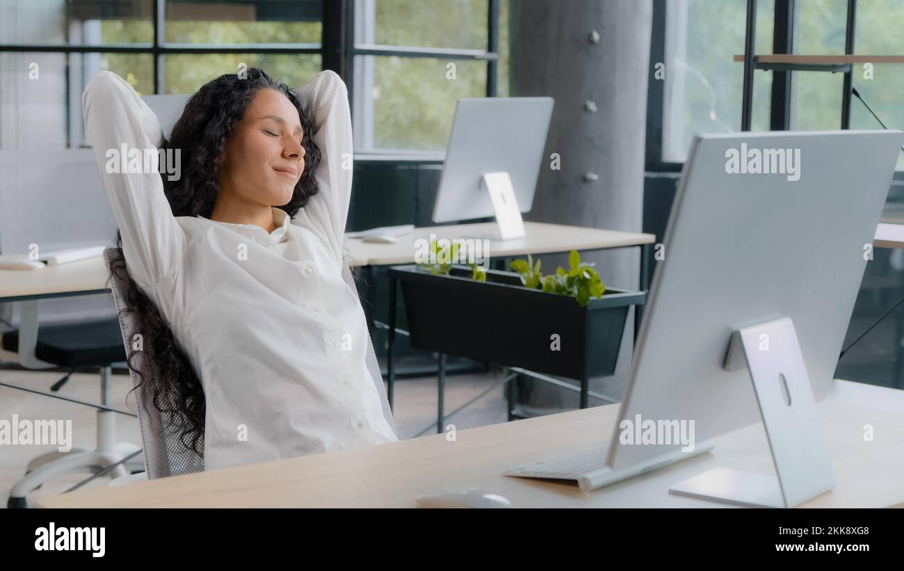 Eine entspannte Managerin, die am Arbeitsplatz eine Pause macht und nach der Arbeit die Hände hinter dem Kopf hält und mit geschlossenen Augen am Schreibtisch sitzt und träumt Stockfoto