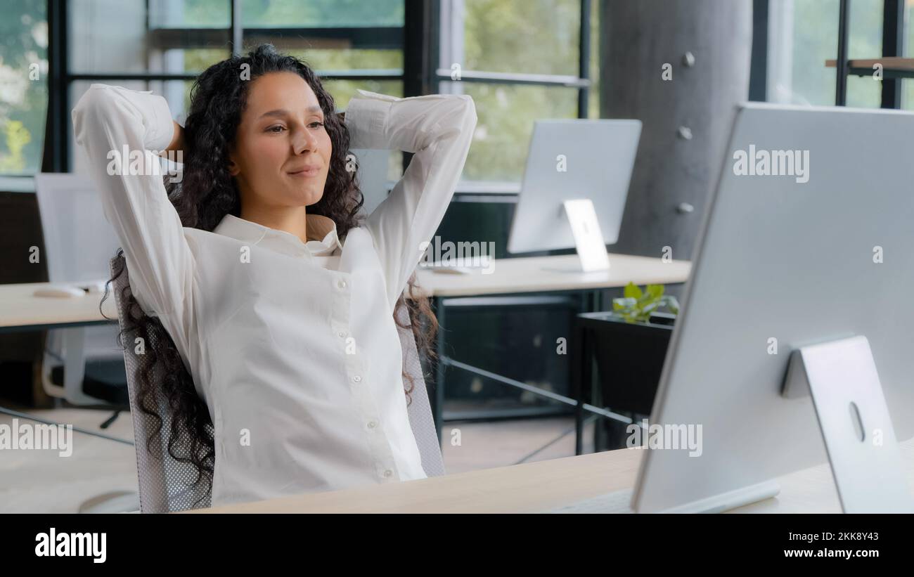 Entspannte, zufriedene junge Frau, die am Arbeitsplatz sitzt und ihre Arbeit genießt, glückliche, ruhige Geschäftsfrau, die sich in den Stuhl lehnt und die Hände hinter dem Kopf hält Stockfoto
