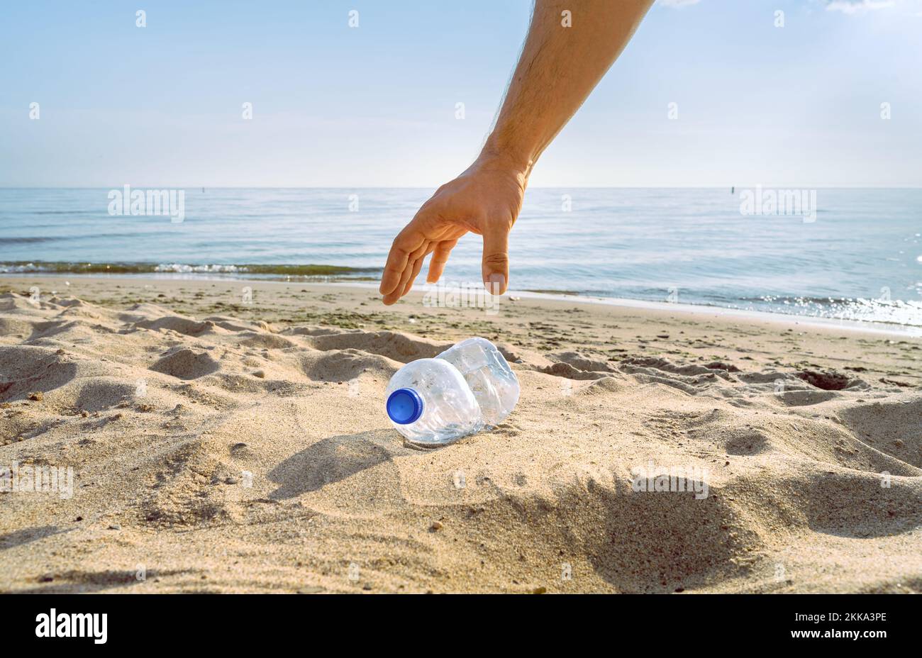 Eine Hand greift, um eine ausrangierte Wasserflasche am Strand abzuholen Stockfoto