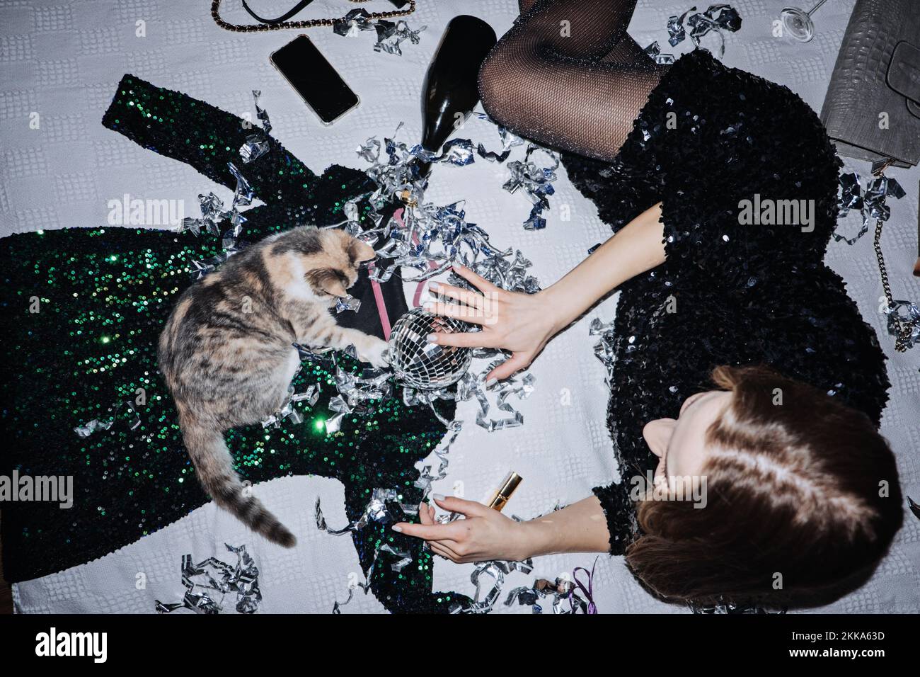 Fröhliche Partyfrau, die auf dem Bett neben einem Disko-Ball-Glitzer-Konfetti liegt und zu Hause Geburtstag oder Neujahrsfeier feiert. Heim, feierlich, verrückter, flippiger Abend Stockfoto
