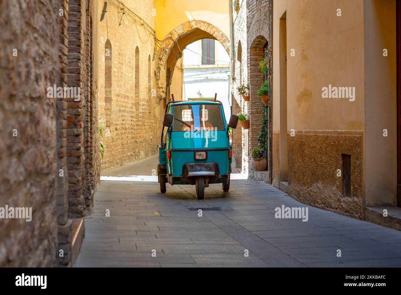 Mann in einem azul-blauen Dreirad, der durch die engen Gassen der alten italienischen Stadt Spello in Perugia fährt. Stockfoto