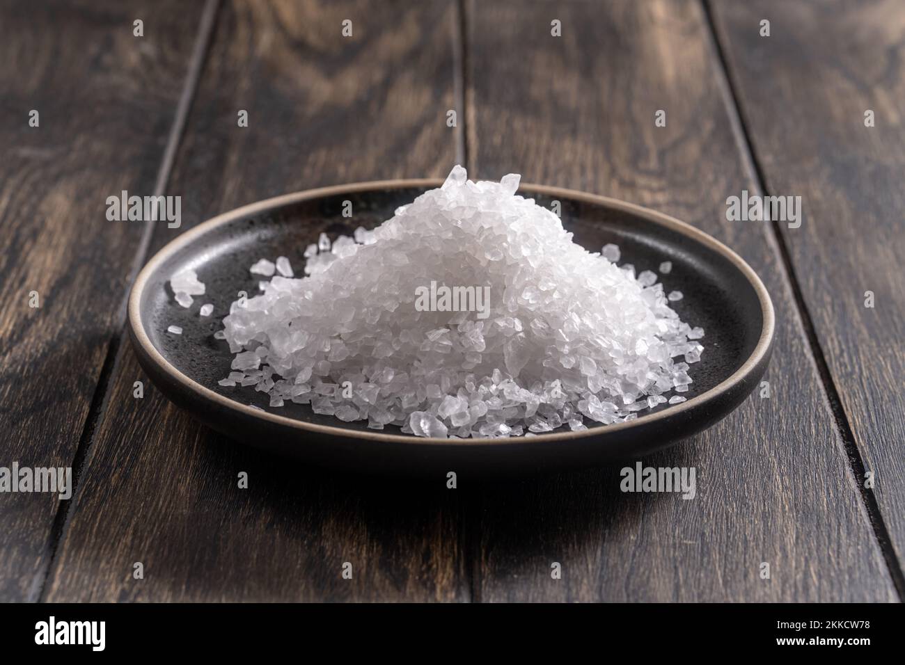 Grobes Salz auf dunkler Platte auf Eichentisch-Nahaufnahme Stockfoto