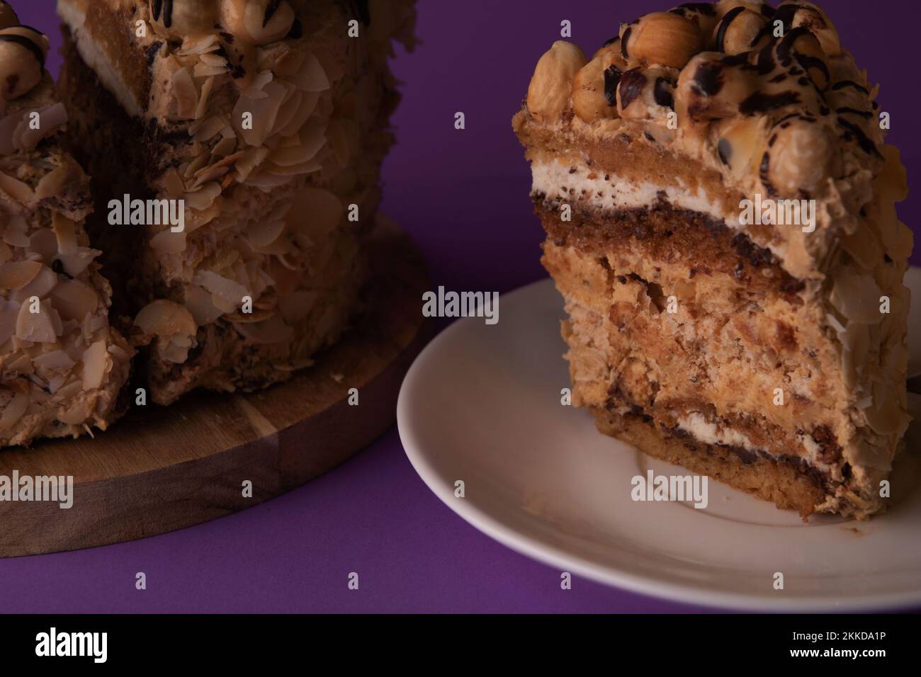 Foto eines geschnittenen Stücks Walnusskuchen auf einer weißen Untertasse im Hintergrund des Kuchens auf einem Holzbrett Stockfoto