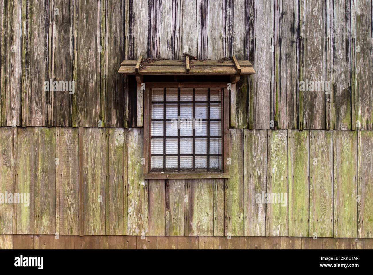 Fenster einer alten Holzhütte. Das im Bild dargestellte Fenster hat ein Holzgitter und ein kleines Fensterdach. Stockfoto Fenster einer alten Holzhütte. Das im Bild dargestellte Fenster hat ein Holzgitter und ein kleines Fensterdach. Stockfoto