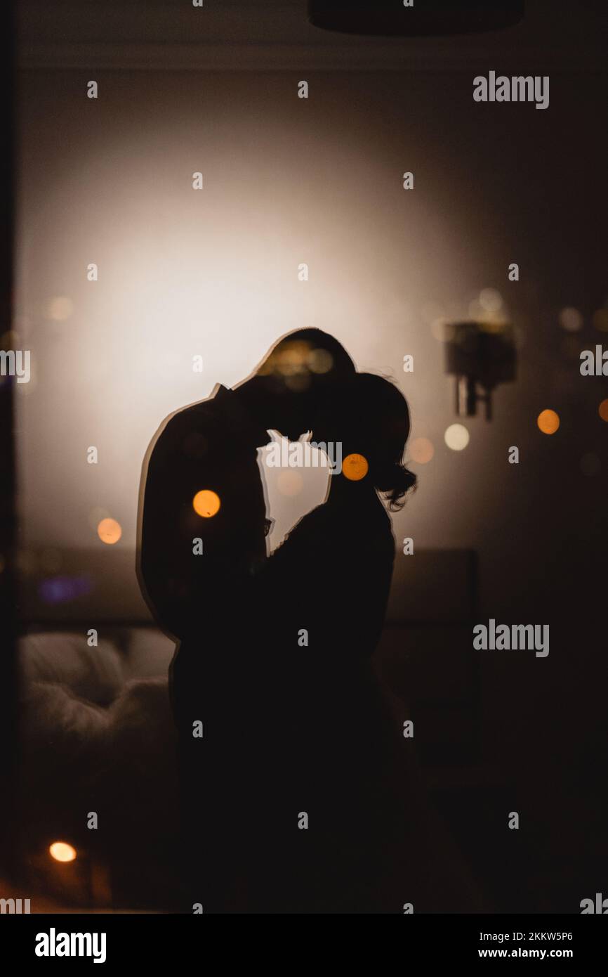 Reflektiert von liebevollem Paar, das sich auf einem Panoramafenster küsst und bei Nacht einen Blick auf die Stadt hat. Romantik-in-the-Sky-Konzept Stockfoto