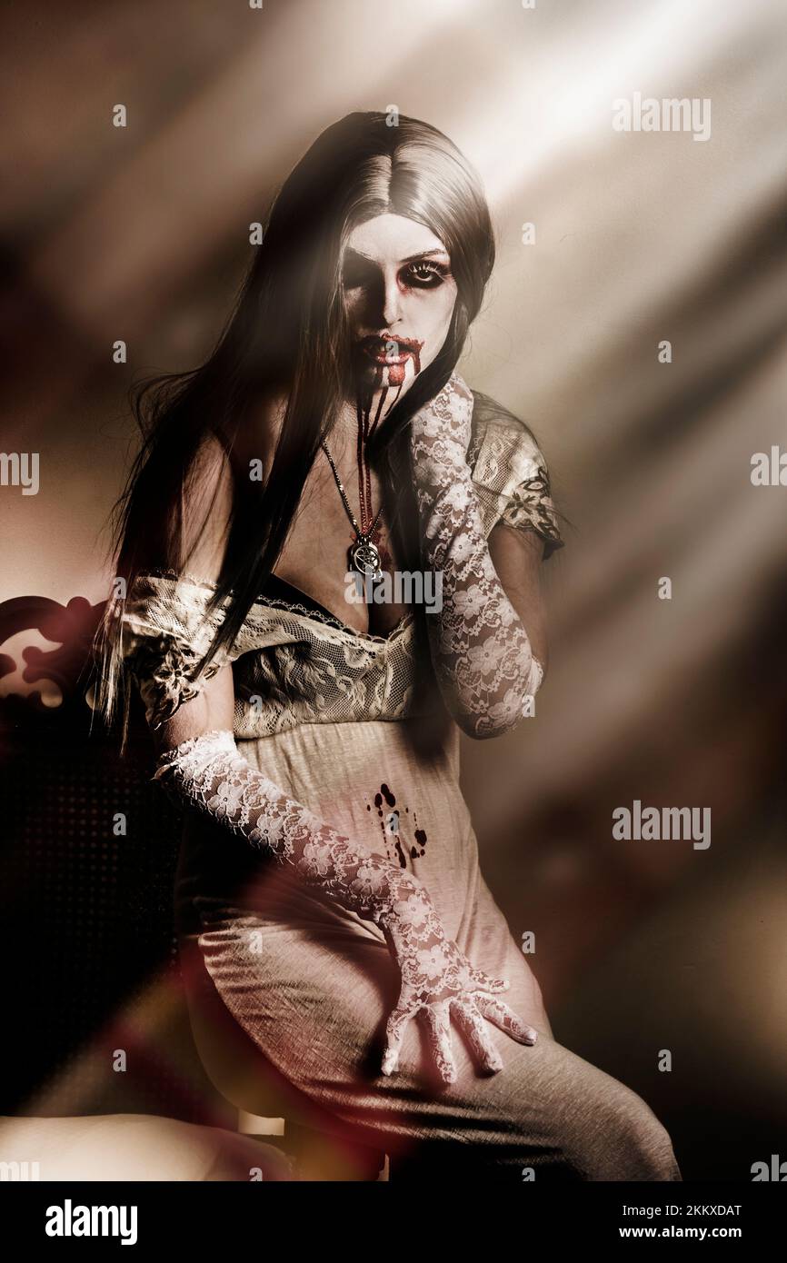 Gruselige Fantasie Foto von einem gotischen weiblichen Vampir mit Blut befleckt Mund sitzen unter Fenster Mondlicht während halloween Stockfoto