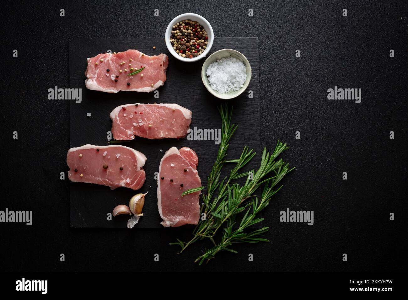 Rohes Fleisch in Scheiben mit Gewürzen und Rosmarin auf Schiefertafeln Stockfoto