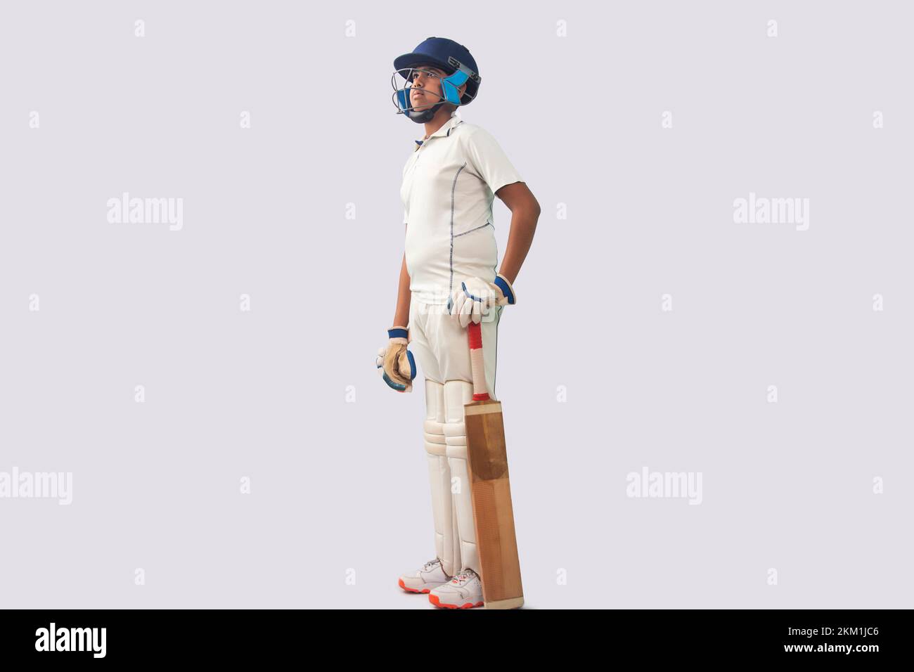 Seitenansicht eines Jungen in Cricket-Uniform mit Fledermaus, der woanders hinschaut Stockfoto