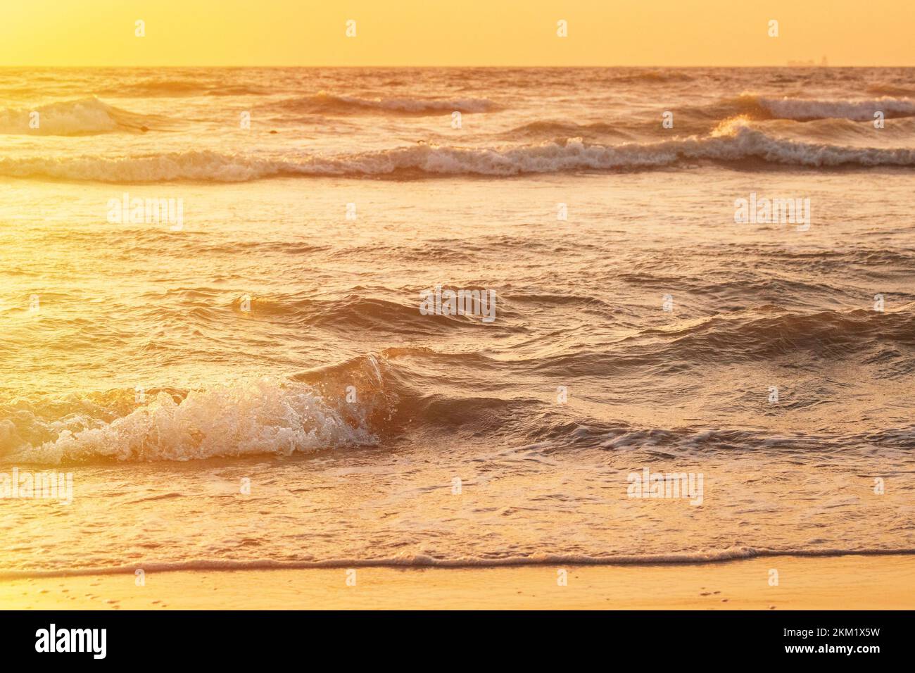 Sonnenuntergang über dem Meer. Natürlicher Sonnenaufgang, warme Farben über dem Meer mit kleinen Wellen. Ozeanwasser Schaum Spritzwasser Sandstrand bei Sonnenuntergang Stockfoto